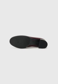 Red leather shoe with a low heel, featuring a textured black rubber sole and smooth upper. No visible patterns or additional hardware.
