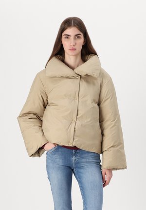 Beige cropped pufferjakke med en stor krave, prydet med trykknapper og en glat, let skinnende tekstur. Bæret med blå jeans.