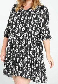 Robe noire à fleurs blanches, col en V, manches trois-quarts et ourlet évasé. Fabriquée en tissu léger avec un design fluide.