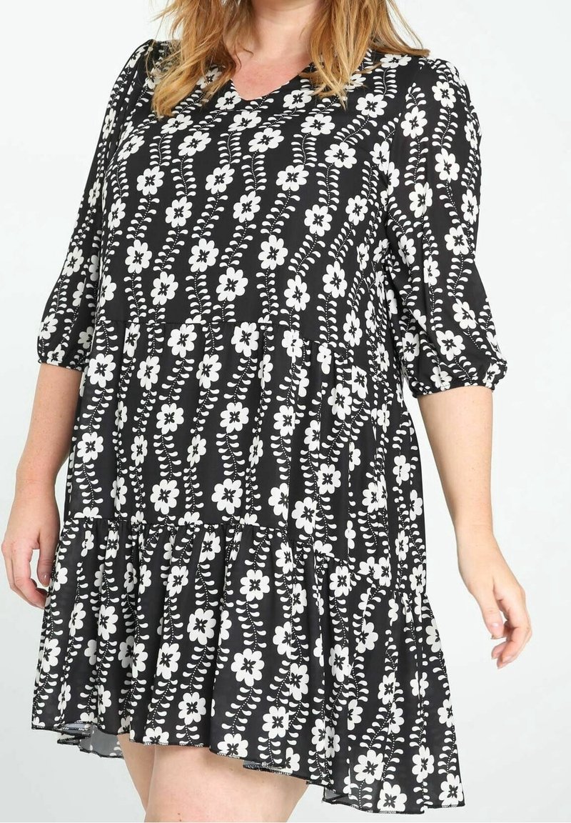 Robe noire à fleurs blanches, col en V, manches trois-quarts et ourlet évasé. Fabriquée en tissu léger avec un design fluide.