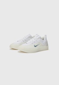 Baskets blanches avec une texture lisse, semelle translucide et un discret swoosh bleu de Nike. Équipées d'un système de laçage et d'un col rembourré.
