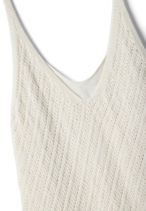 Haut sans manches en tricot crème avec un col en V et un motif subtil en ajour diagonal sur le tissu.