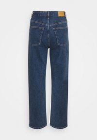 Mörkblå jeans med raka ben, bakfickor och ett brunt lädermärke med varumärket på midjebandet, visade bakifrån.