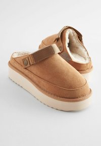 Barna velúr klumpák puha béléssel, slip-on stílus, állítható pánt és vastag, textúrált fehér talp.