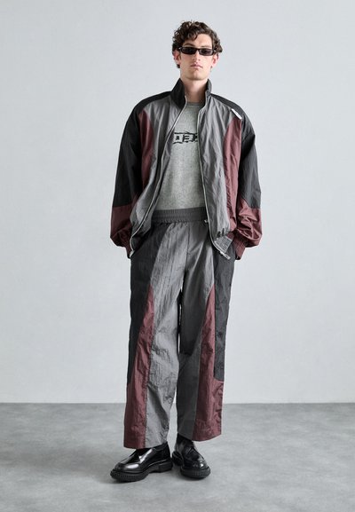 Ensemble de sport composé d'un survêtement gris et bordeaux, avec une veste zippée et un pantalon ample en tissu texturé, accompagné de chaussures noires.