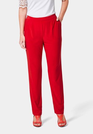 Pantalons rouges fluides avec une coupe décontractée, dotés d'une taille plate et de poches latérales, associés à des chaussures à talons ouverts corail.