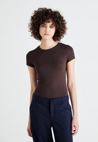 Brown fitted short-sleeve T-shirt made of lightweight cotton fabric, paired with navy tailored trousers, with a round neckline and minimal design.