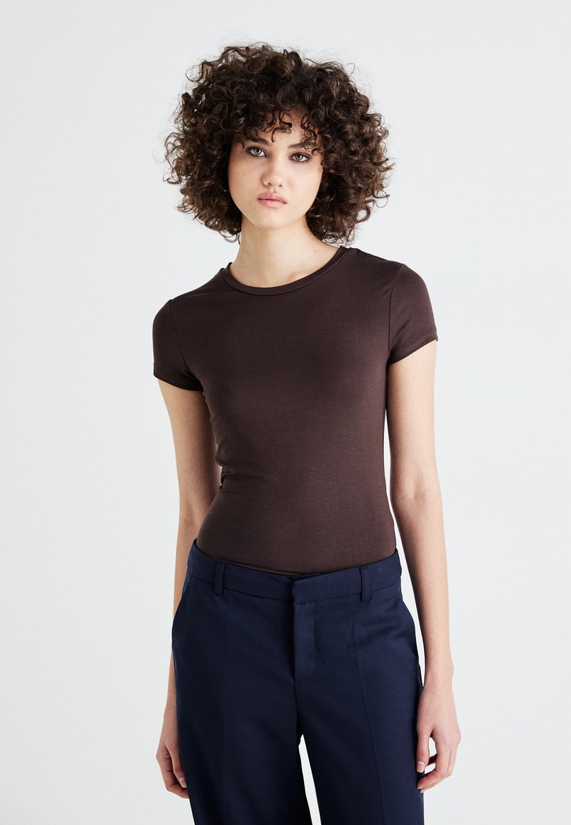 Brown fitted short-sleeve T-shirt made of lightweight cotton fabric, paired with navy tailored trousers, with a round neckline and minimal design.
