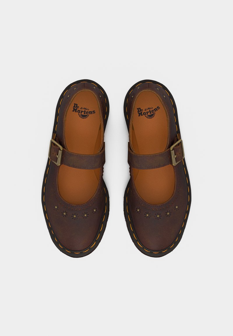 Brown leather Mary Jane-style Dr. Martens shoes with floral perforations, adjustable buckle straps, and yellow-stitched thick soles.