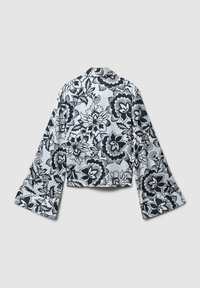 Camicia bianca a maniche lunghe con ampi polsini e motivo floreale nero, mostrata dal retro su uno sfondo grigio chiaro.