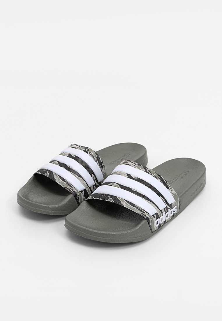 Para szarych klapków Adidas z białymi paskami w trzy paski i wzorem w kamuflaż na pasku, ustawionych pod kątem na białym tle.