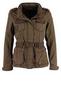 Giacca militare marrone con due tasche sul petto, vita con cintura, collo alto e tasche laterali con zip. Realizzata in tessuto leggero.