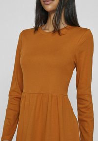 Ribbade långärmade klänning i en varm orange nyans. Har en figurnära bodice och en utsvängd kjol med en söm i midjan. Slät struktur.