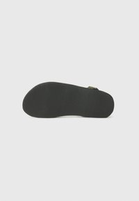 Svart gummisåle til sandaler med en teksturert overflate som har horisontale riller for grep. Bøyd form med åpen design.
