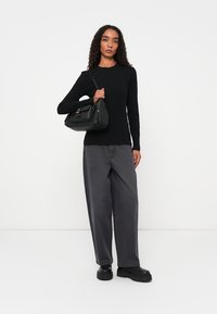 Top negro de manga larga con canalé, jeans gris holgados y zapatos de plataforma negros. La modelo sostiene un bolso negro estructurado con detalles dorados.