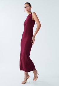 Mauve fitted sleeveless dress with a scoop neckline, smooth texture, and long silhouette. Paired with strappy gold high heels.