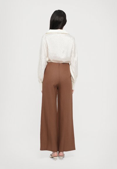 Bluză crem cu model texturat și guler, asortată cu pantaloni largi maro cu talie înaltă. Pantalonii au un fermoar discret la spate.