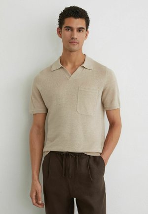 Fiatal férfi göndör sötét hajjal, bézs színű, galléros, zsebes rövid ujjú kötött ingben és sötétbarna, zsinóros nadrágban.