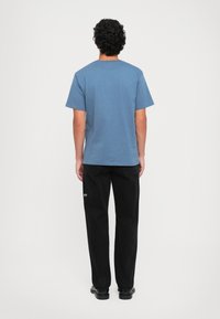Tricou albastru cu mânecă scurtă și guler rotund, asortat cu pantaloni negri lejeri. Design simplu, textură moale și detalii minime.