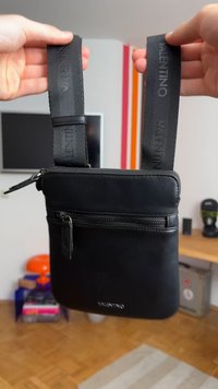 Borsa a tracolla nera con una texture liscia, dotata di una tasca con zip, spallacci regolabili con il marchio "VALENTINO" e forma rettangolare.