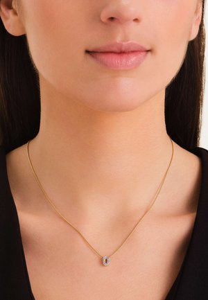 Collar de oro con una cadena delgada que presenta una piedra ovalada negra rodeada de pequeñas piedras transparentes. Diseño simple con una textura suave.