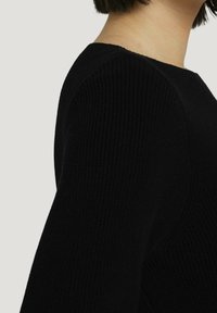 Czarny sweter dzianinowy o prążkowanej strukturze, klasycznym okrągłym dekolcie i dopasowanej sylwetce, podkreślający miękkość i formę odzieży.