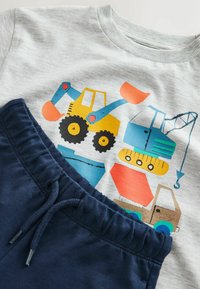 T-shirt gris clair pour tout-petit avec imprimé coloré de véhicules de chantier, associé à un pantalon bleu marine à taille élastique avec cordon.