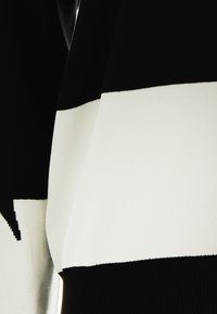 Maglione lavorato a maglia con audaci righe orizzontali bianche e nere, texture liscia e vestibilità comoda. Presenta un motivo di dettaglio contrastante.
