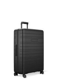 Black hard-shell suitcase with vertical grooves, retractable handle, and four spinner wheels for mobility. Smooth texture and minimalist design.