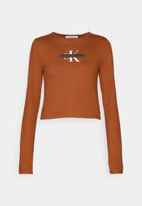 Dlouhý rukáv, zkrácená košile v rezavé barvě, vyrobená z hladkého materiálu, s černobílým logem Calvin Klein uprostřed.