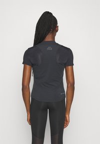 Camiseta atlética de manga corta negra con un diseño ajustado, que presenta paneles de malla en los hombros y un logo cerca del escote.