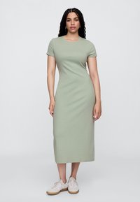 Sukienka maxi z jasnej zielonej bawełny, dopasowany krój z krótkimi rękawami, okrągły dekolt, gładka faktura, noszona z beżowymi sneakersami.