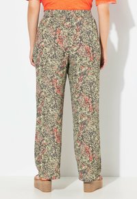 Donna che indossa pantaloni a vita alta e larghi con un motivo astratto verde e corallo, abbinati a un top corallo e sandali con zeppa.