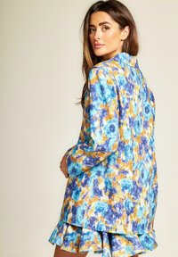 Blazer colorato con un motivo floreale in tonalità di blu, arancione e bianco. Presenta maniche lunghe, un colletto e un orlo inferiore arricciato.