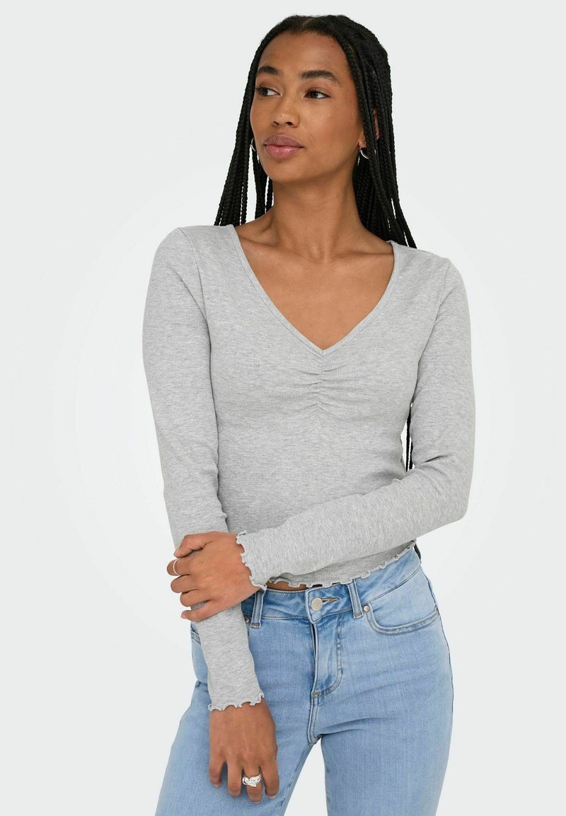 Top grigio a maniche lunghe con scollo a V, caratterizzato da dettagli arricciati sul petto e polsini a onde. Il tessuto ha una finitura morbida e testurizzata.