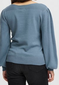 Niebieski sweter dzianinowy z szerokim dekoltem, prążkowanymi mankietami i krawędzią. Tył ma gładką fakturę i lekkie bufiaste rękawy.