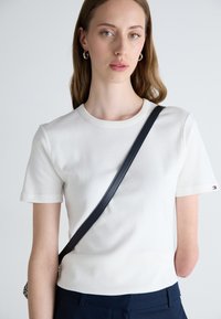 Hvit kortermet t-skjorte laget av mykt stoff, med rund hals, ren design og en liten logo på ermet. Mørk bagstropp synlig.