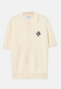 Polo crème à manches courtes avec deux boutons et un écusson logo noir en forme de losange avec un "L" blanc sur la poitrine gauche.