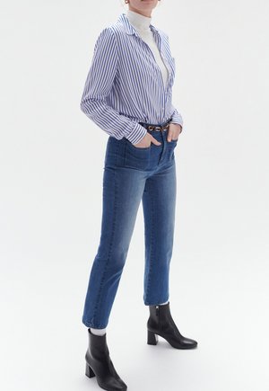 Camicia a maniche lunghe a righe blu e bianche, jeans azzurri a vita alta e stivaletti neri con tacco quadrato e dettaglio con zip.
