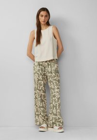 Lichtbeige mouwloos topje gecombineerd met losse groene geblokte broek met grote crèmekleurige bladeren en romige chunky sandalen.