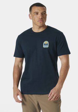 Camiseta de algodón azul marino con cuello redondo. Cuenta con un pequeño parche de logo colorido en la parte izquierda del pecho. Mangas cortas, corte regular.