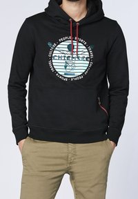 Svart huvtröja i mjukt tyg med ett grafiskt tryck på framsidan, med färgade detaljer och en dragkedjeficka på sidan.