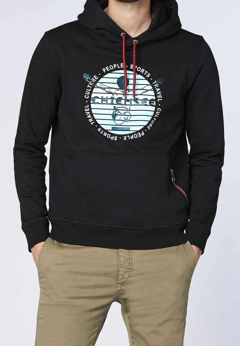 Svart huvtröja i mjukt tyg med ett grafiskt tryck på framsidan, med färgade detaljer och en dragkedjeficka på sidan.