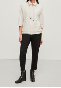 Lys beige zip-jakke med høj krave, trekvartærmer, parret med sorte tapered bukser og sorte ankelstøvler med spænder.