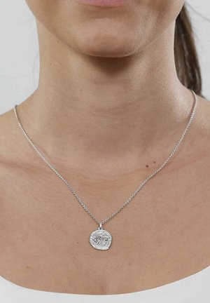 Silver chain necklace with a round, textured pendant featuring an engraved animal design worn on a woman's neck and upper chest.