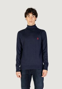 Maglione a collo alto blu in tessuto morbido con orlo e polsini a coste, caratterizzato da un piccolo logo rosso sul lato sinistro del petto.