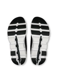 Semelles de chaussures de sport en noir et blanc avec un motif texturé. Comprend des sections en caoutchouc segmentées pour l'adhérence et le confort. Étiquette de marque visible.