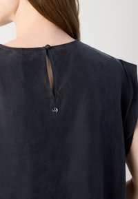 Garbamento blu scuro realizzato in un tessuto morbido e testurizzato. Presenta un foro a chiave sul retro, chiuso con un piccolo bottone. Maniche corte.