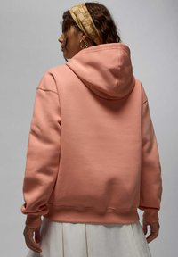 Sweat-shirt rose avec capuche, texture douce, épaules tombantes, poignets côtelés et coupe décontractée, présenté sur un fond neutre.