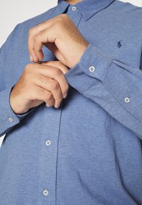 Koszula z kołnierzykiem na guziki w jasnoniebieskim materiale, z kołnierzem, długimi rękawami z mankietami na guziki oraz małym logo na piersi.